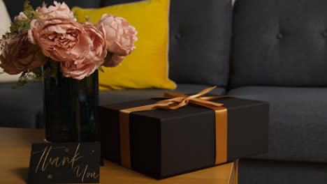 Close-Up-Of-Gift-Wrapped-Present-With-Thank-You-Card-And-Flowers-On-Table-In-Lounge-At-Home